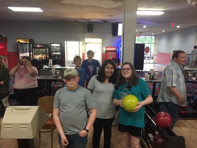 Group standing in an arcade; one person holds a green ball, with arcade machines and bowling balls nearby.