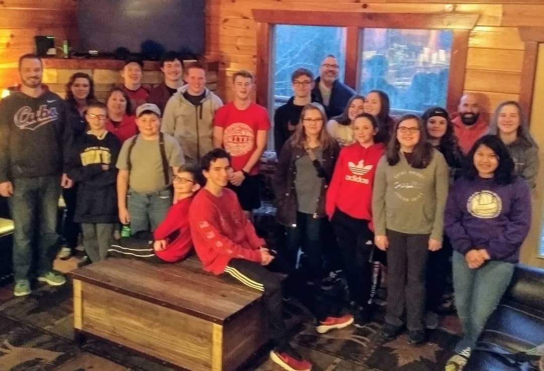 Group of people posing indoors in a rustic wooden room, some seated and some standing.