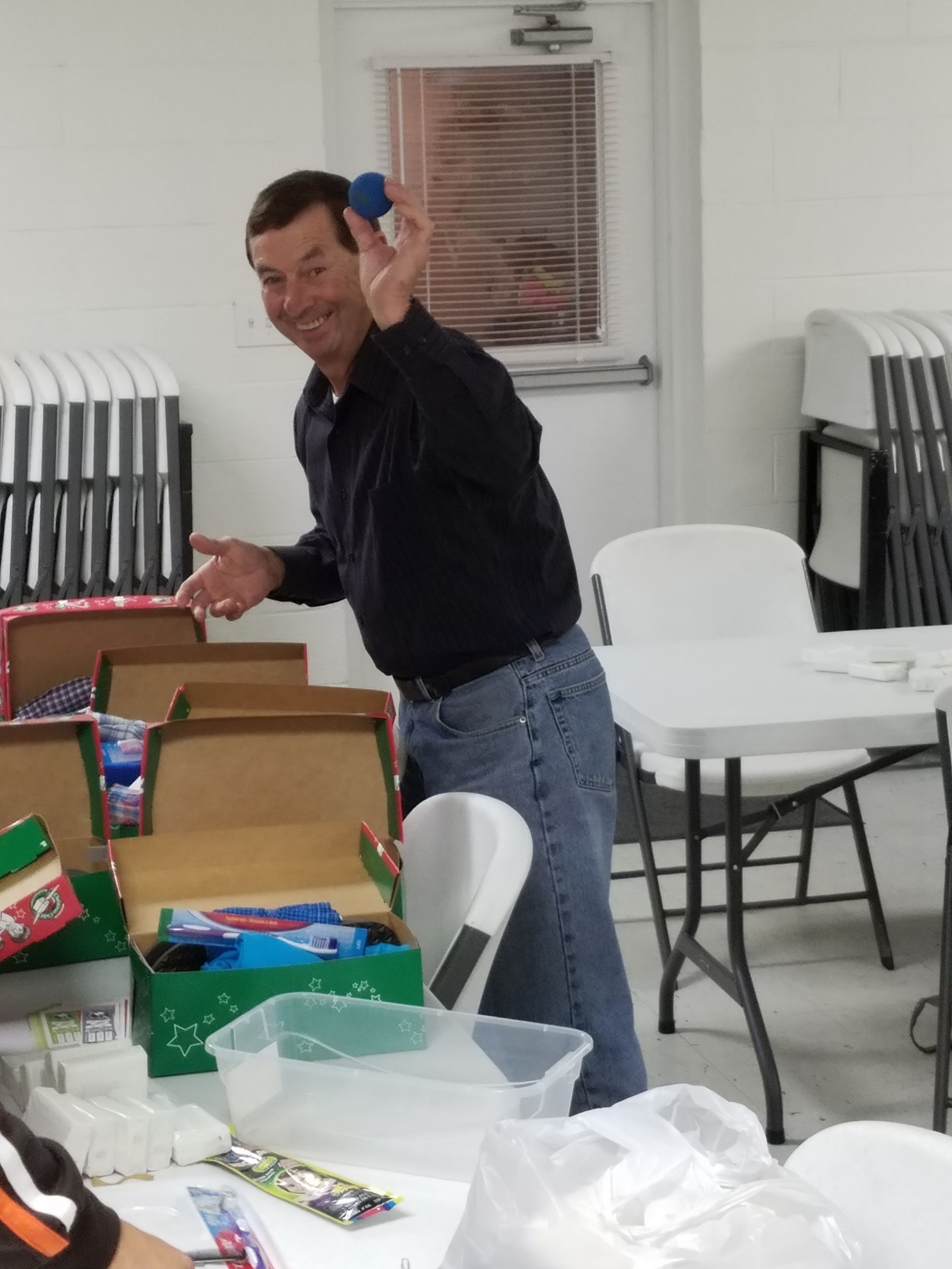 Man tossing a blue object at a table with open boxes and supplies in a bright room