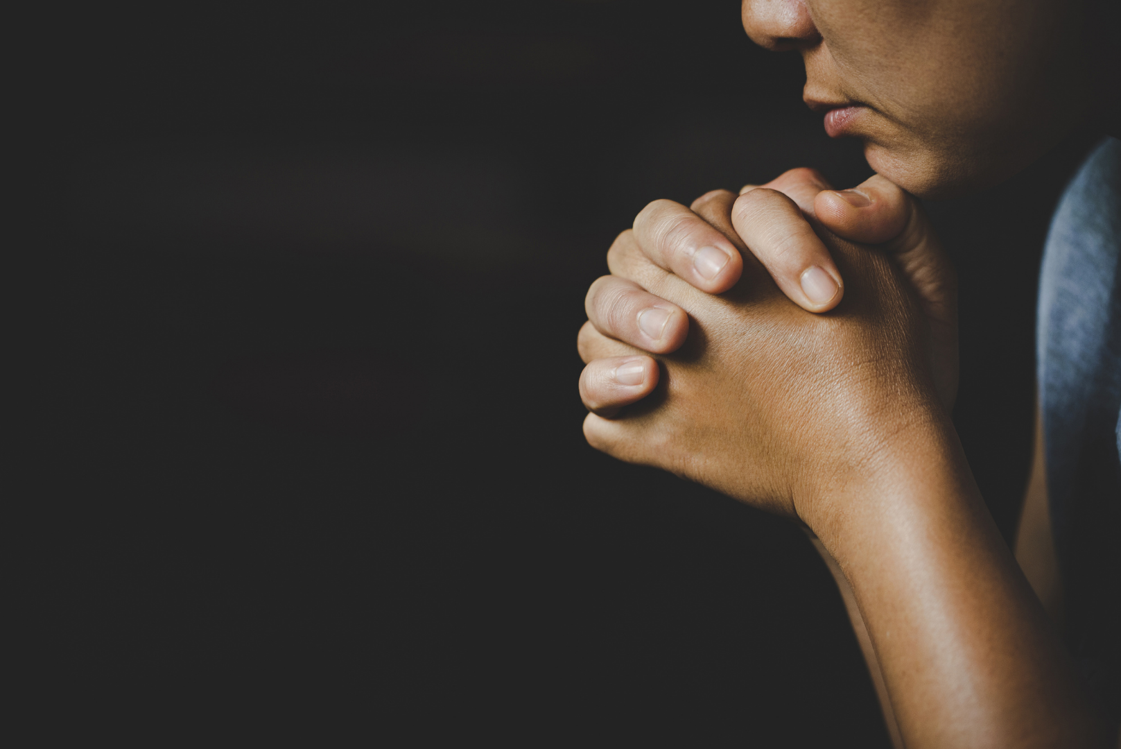 Close-up of clasped hands and a thoughtful face in profile against a dark background