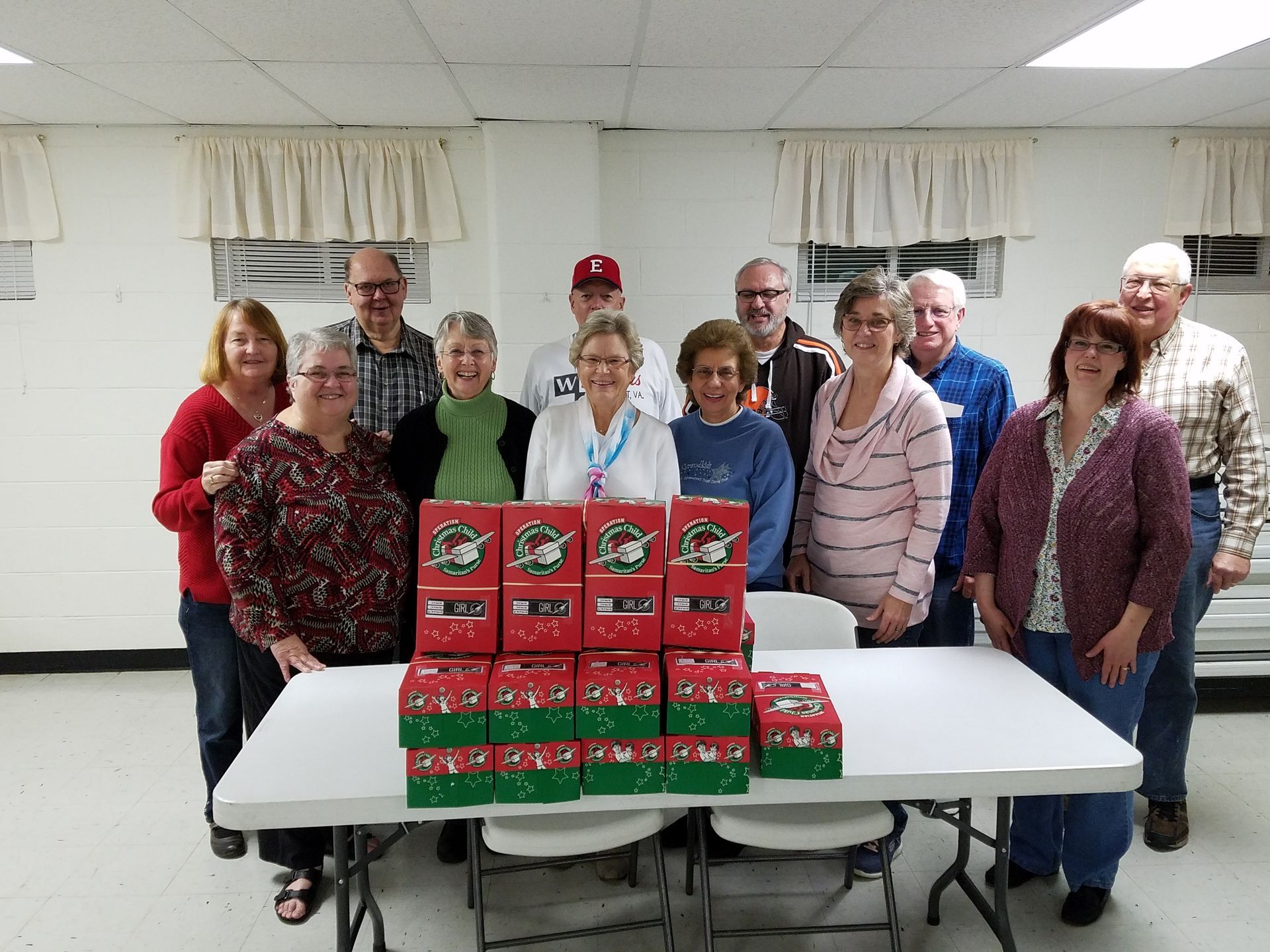 Group of volunteers standing behind stacked red and green boxes on a table in a bright room