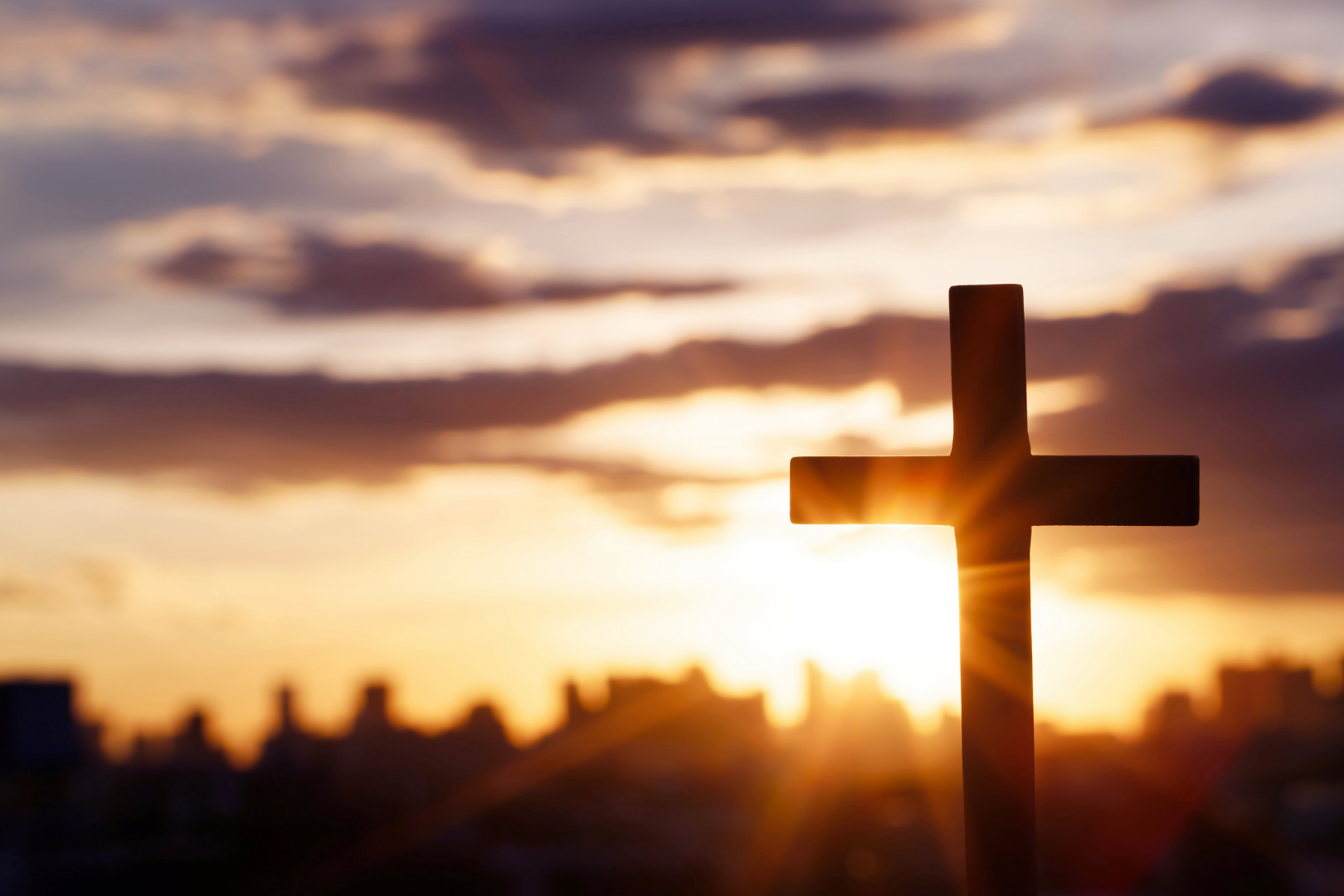 Silhouette of a cross at sunset with a glowing sky and blurred clouds in the background