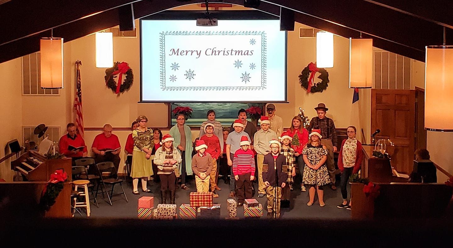 Children in red outfits perform on a decorated holiday stage with a projected festive sign