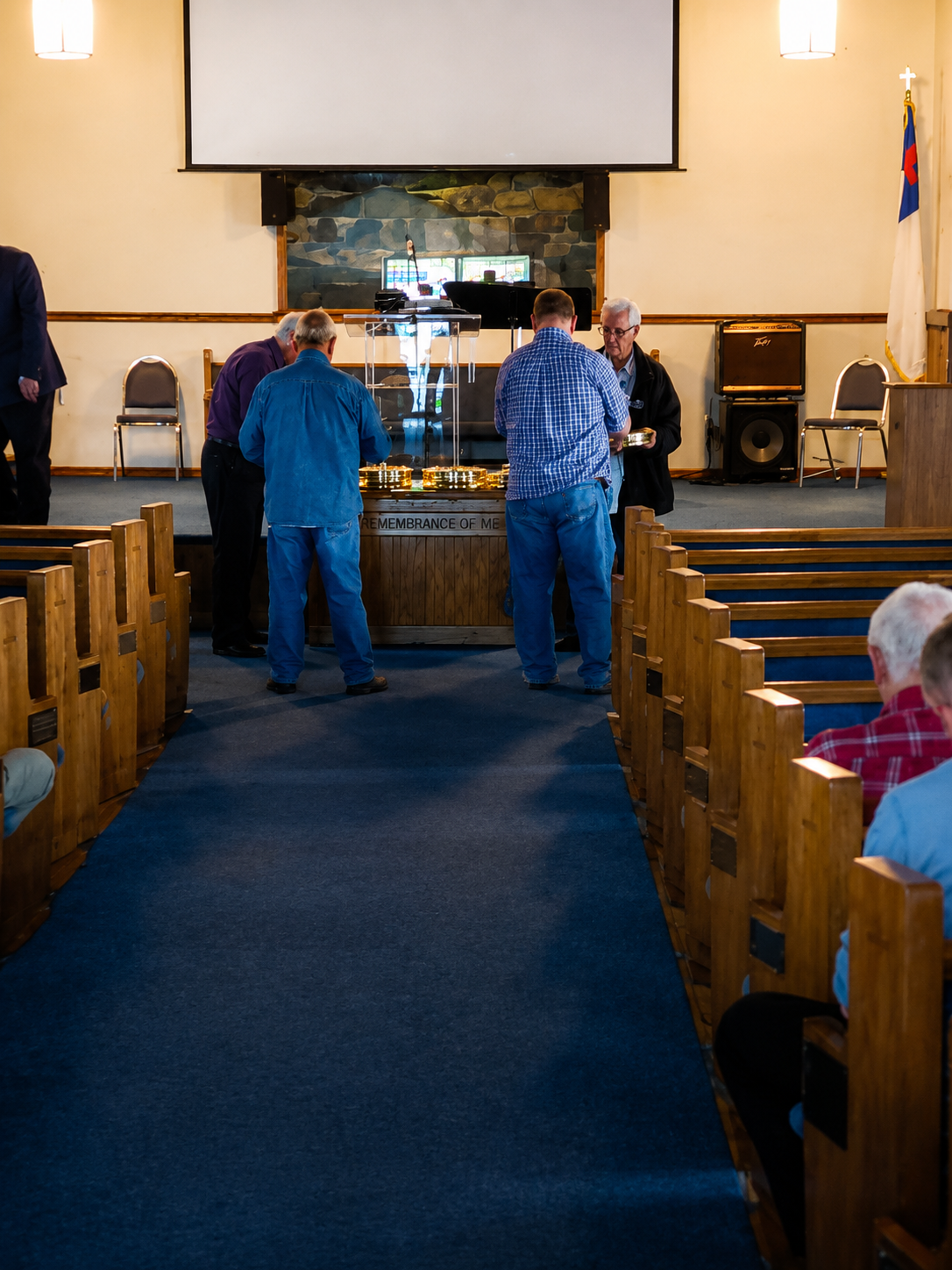 Two people standing in a church aisle facing the altar, with pews and a stained-glass window in the background