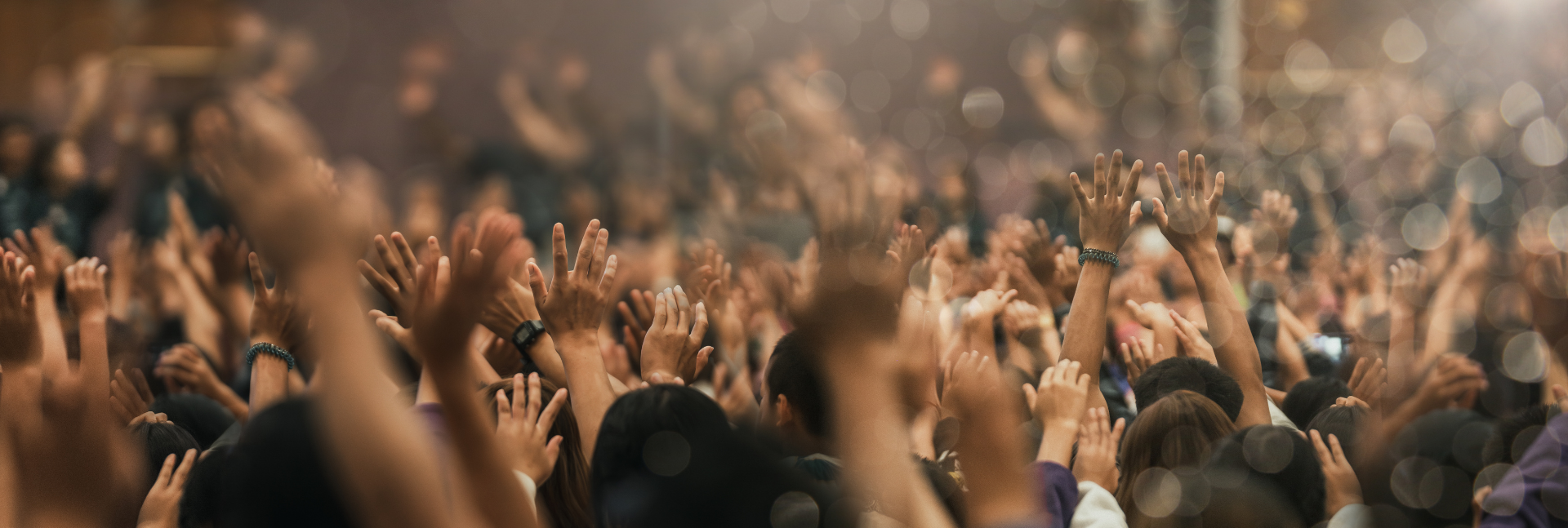 Crowd of people with raised hands at a concert or festival, bathed in warm lights