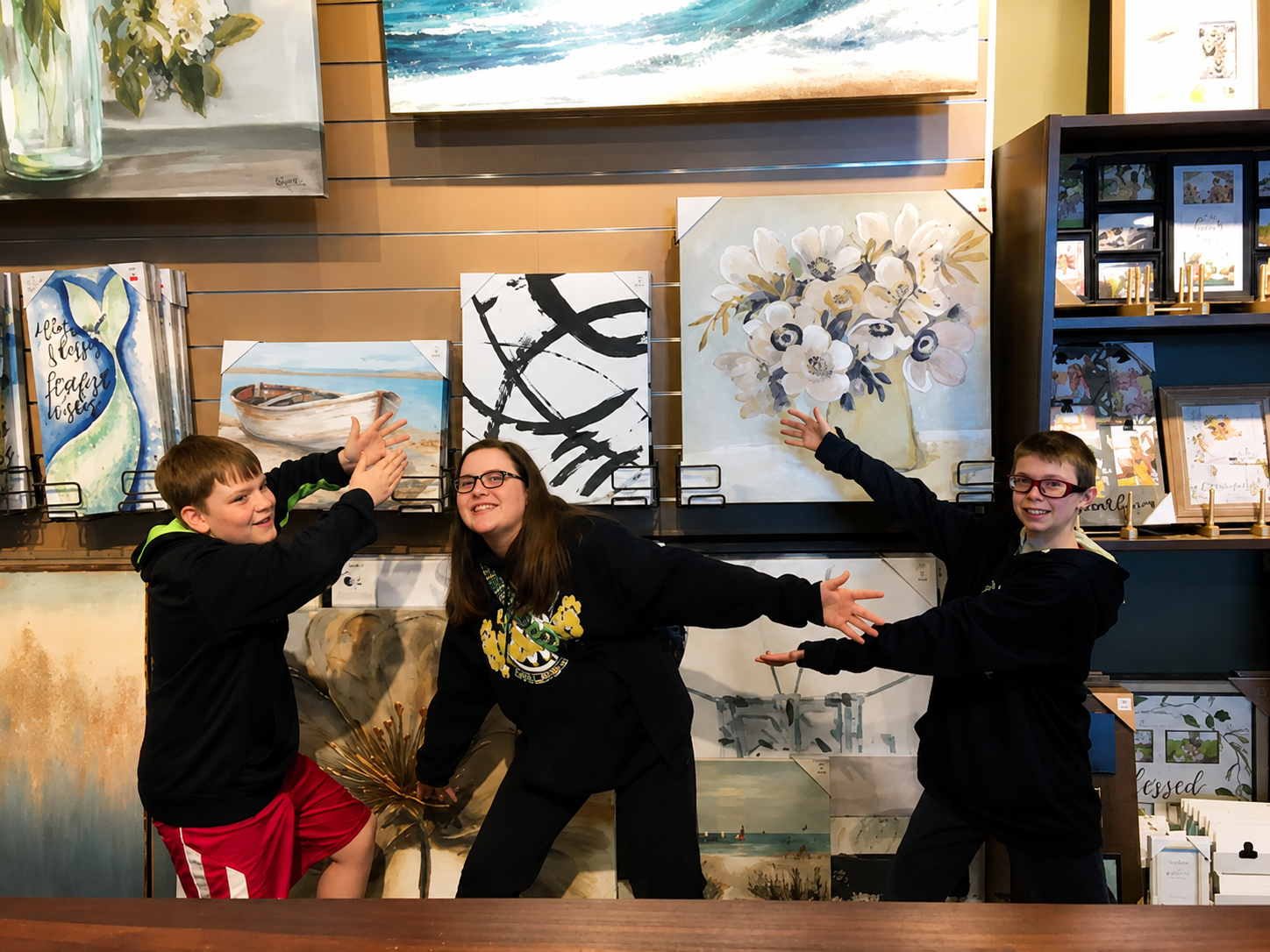 Three people posing playfully in an art gallery beside colorful paintings.