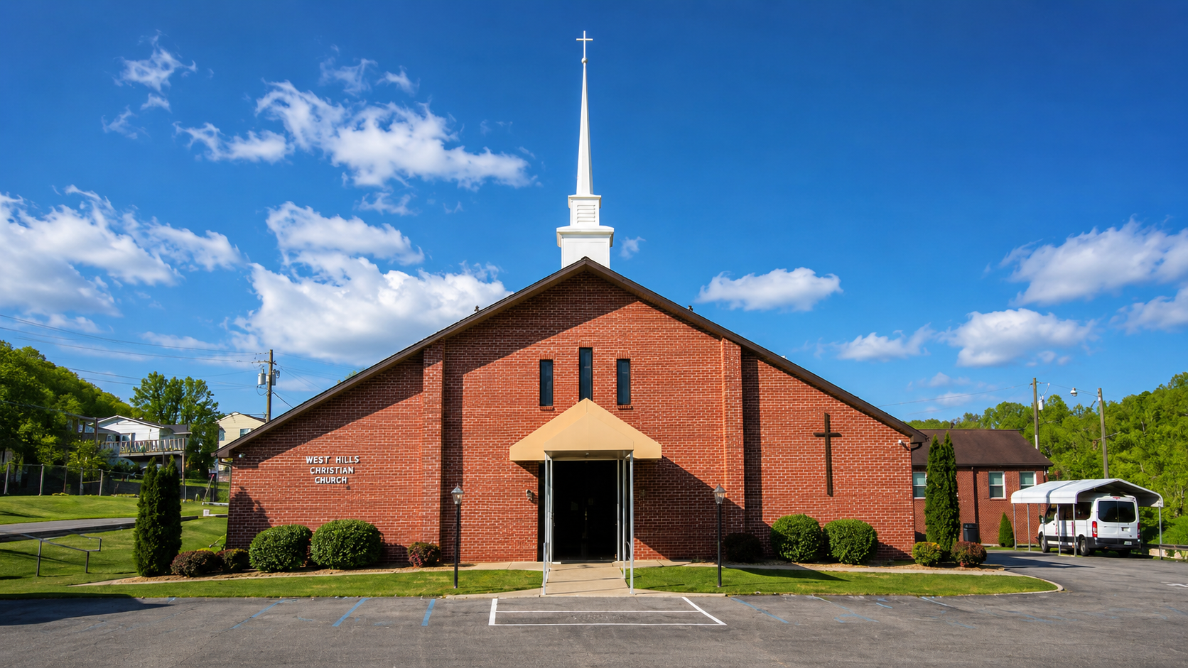 Red brick church with white steeple, centered entrance, and parking lot under a blue sky