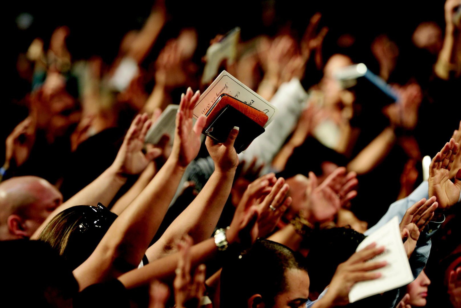 Crowd with raised hands at a concert, one person holding a small book aloft