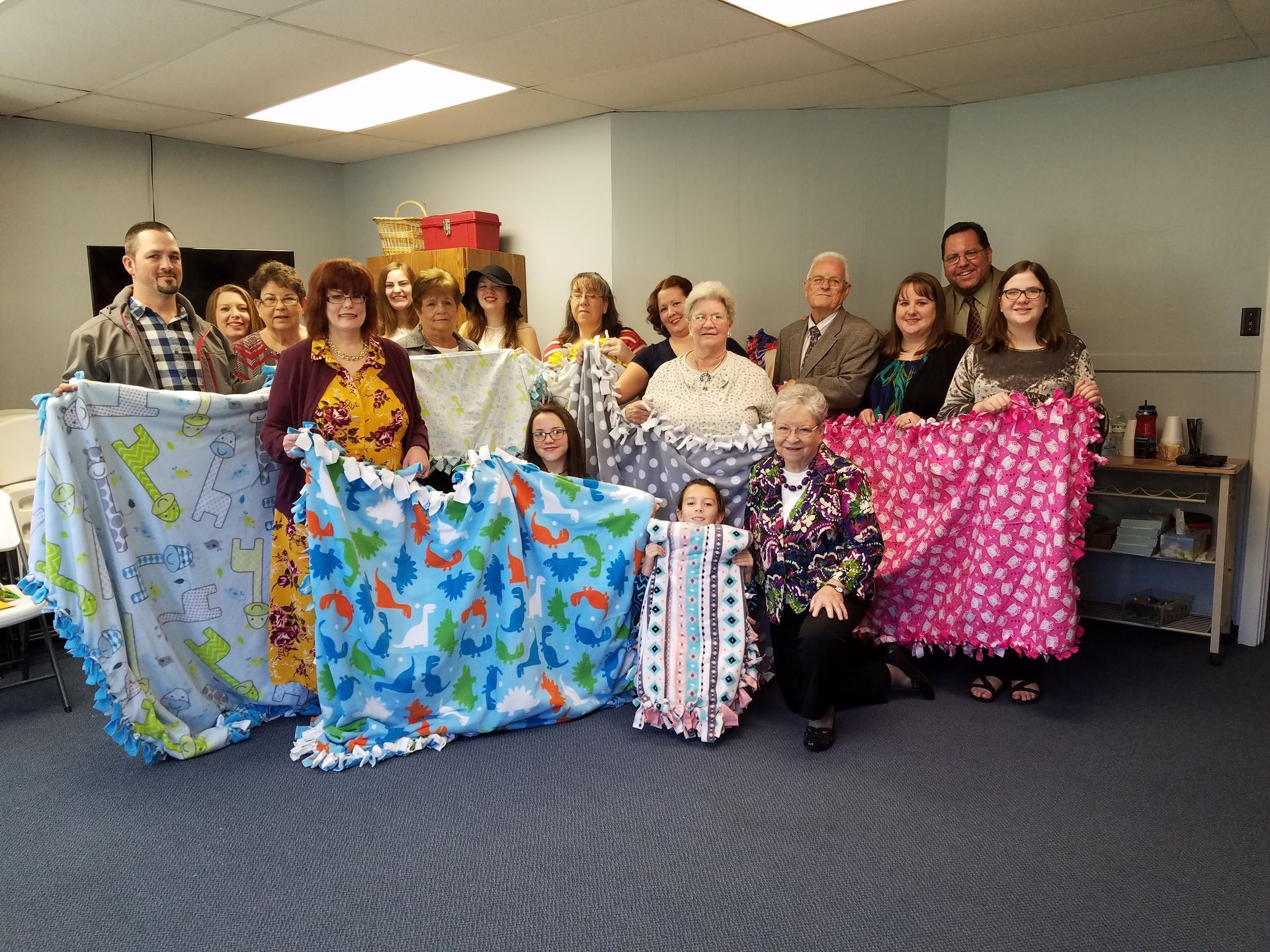 Group of people holding colorful fleece blankets in a room, posing for a photo.
