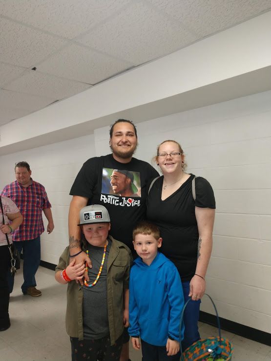 Four people posing indoors in a hallway, with two adults standing behind two children.