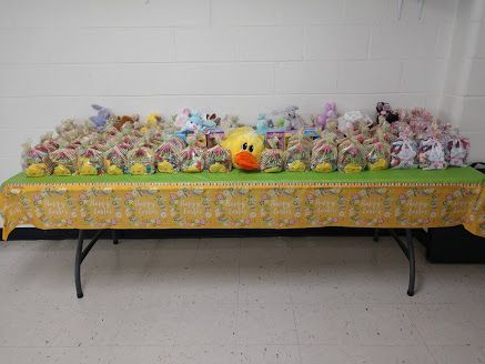 Table covered with many colorful gift bags and a yellow plush toy against a white wall.