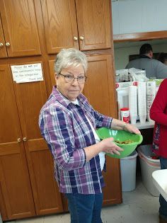 Woman in plaid shirt holding a green bowl in a kitchen with wooden cabinets.