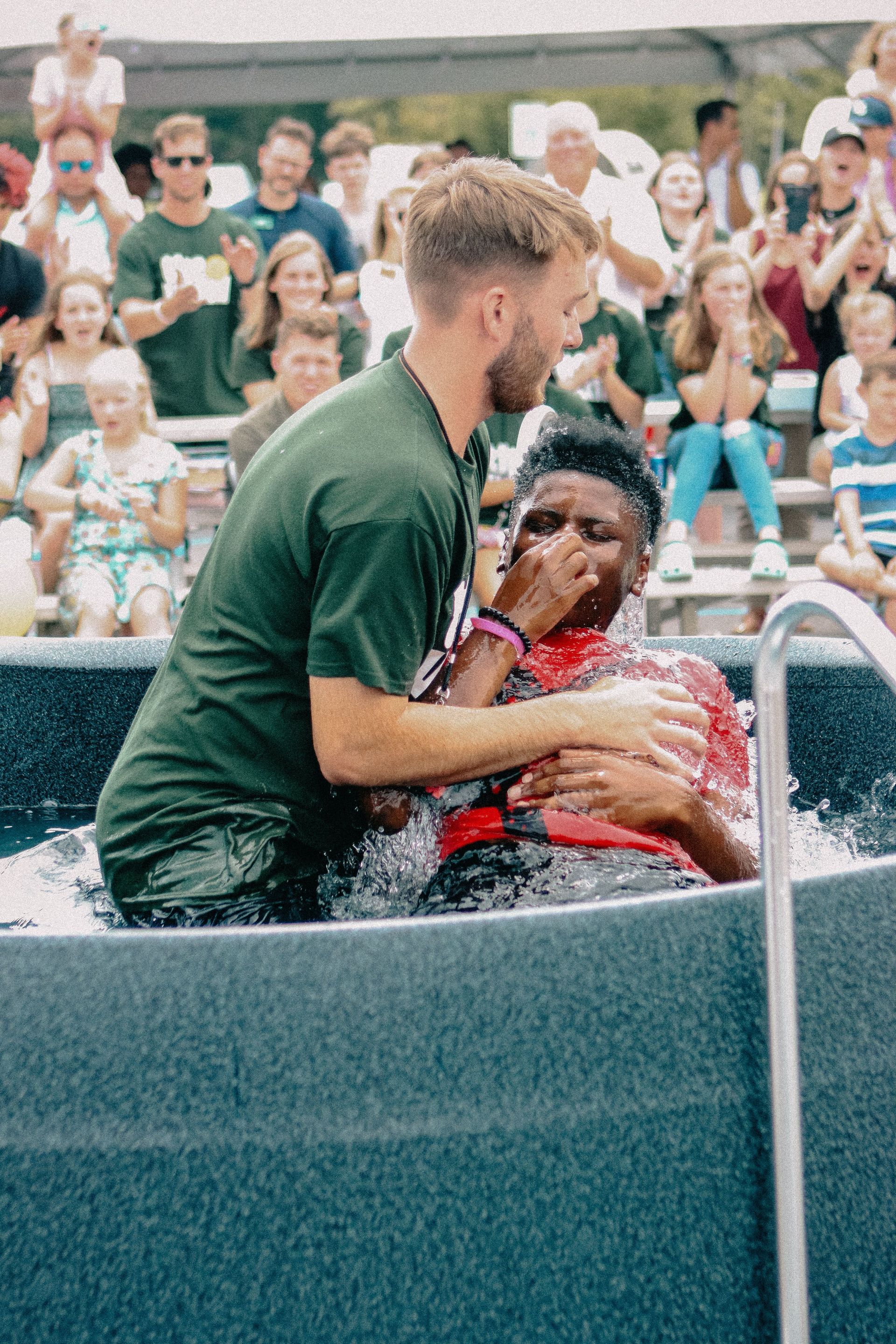 People standing by a pond as a person in white baptizes another in the water