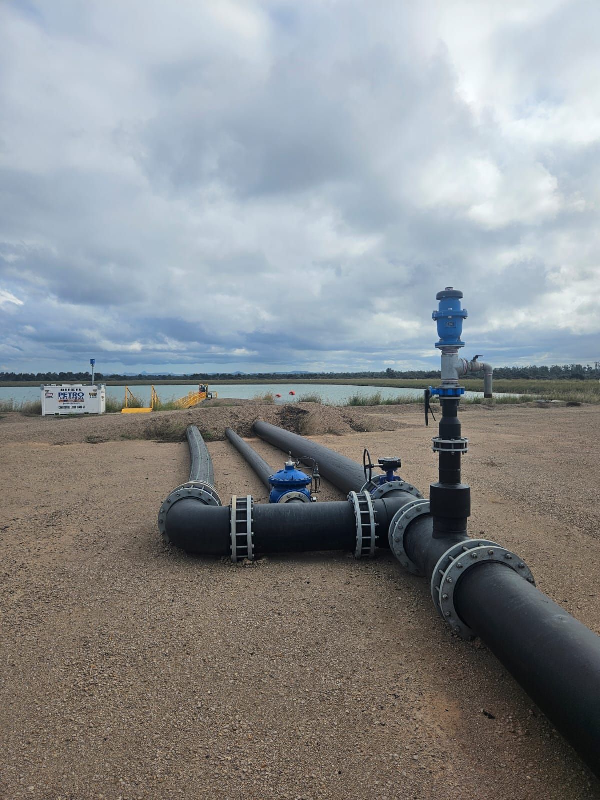 Industrial pipes and a blue valve assembly on a gravel site under a cloudy sky — Forcequip In Mount Isa, QLD
