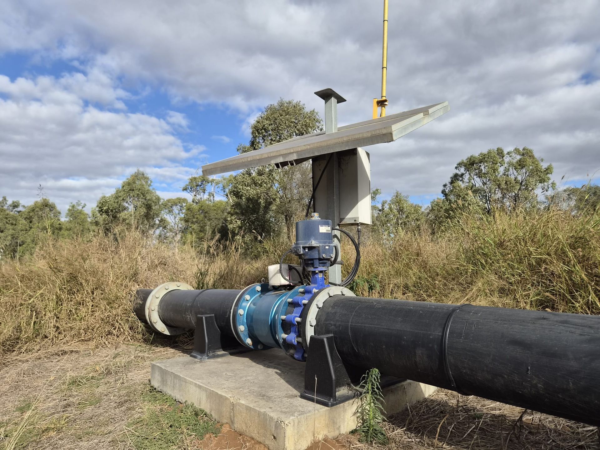 Industrial black pipeline with blue valve and solar-powered sensor station in a grassy field — Forcequip Hire In Mackay, QLD