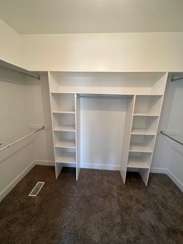 A walk in closet with white shelves and clothes racks in a bedroom.