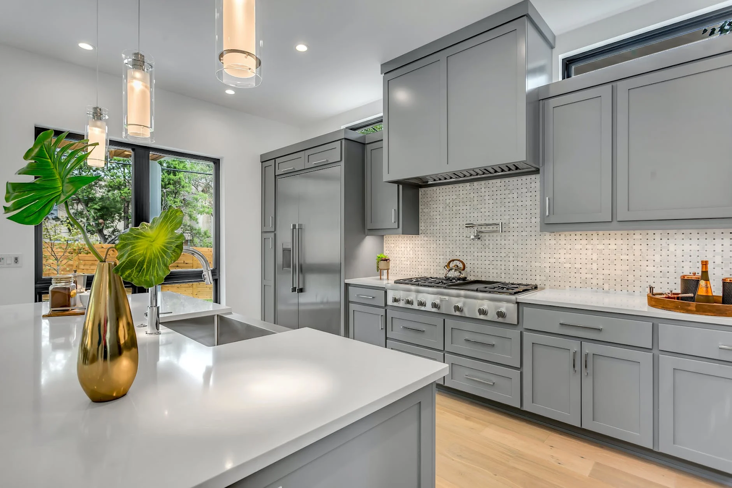 A kitchen with gray cabinets , white counter tops , and stainless steel appliances.