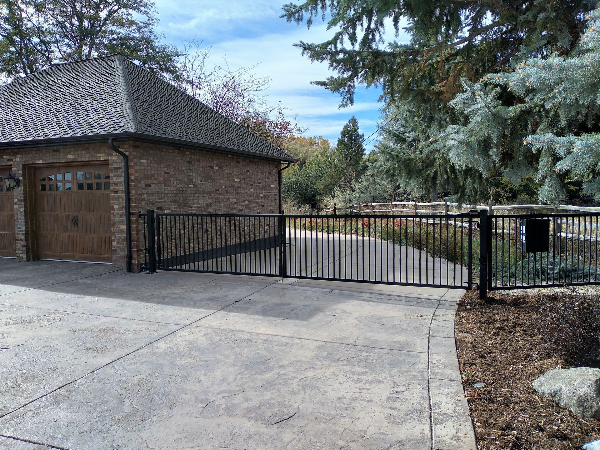 A brick garage with a wooden door is behind a metal gate.