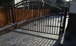 A black metal gate is open to a driveway next to a wooden fence.