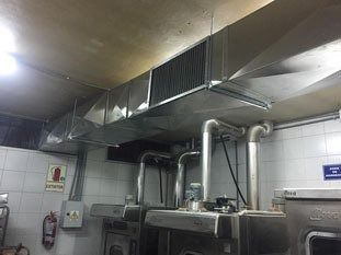 Techo de cocina industrial con grandes conductos de ventilación metálicos sobre los equipos de cocina.