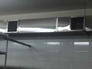 Campana extractora de cocina de acero inoxidable con salidas de ventilación sobre pared de azulejos blancos y estante.