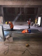 Trabajadores con chalecos naranjas inspeccionando una obra de construcción de hormigón por la noche.