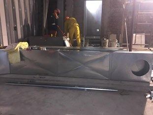 Trabajadores con trajes amarillos inspeccionando una gran estructura metálica gris en el interior.