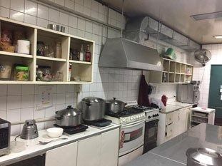 Cocina comercial con gabinetes blancos, estufas de acero inoxidable, ollas y estantes llenos de suministros.