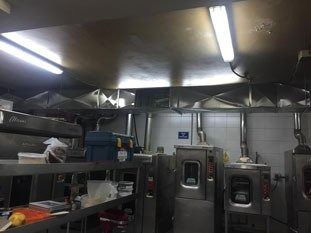 Cocina comercial con electrodomésticos de acero inoxidable y luces cenitales brillantes.