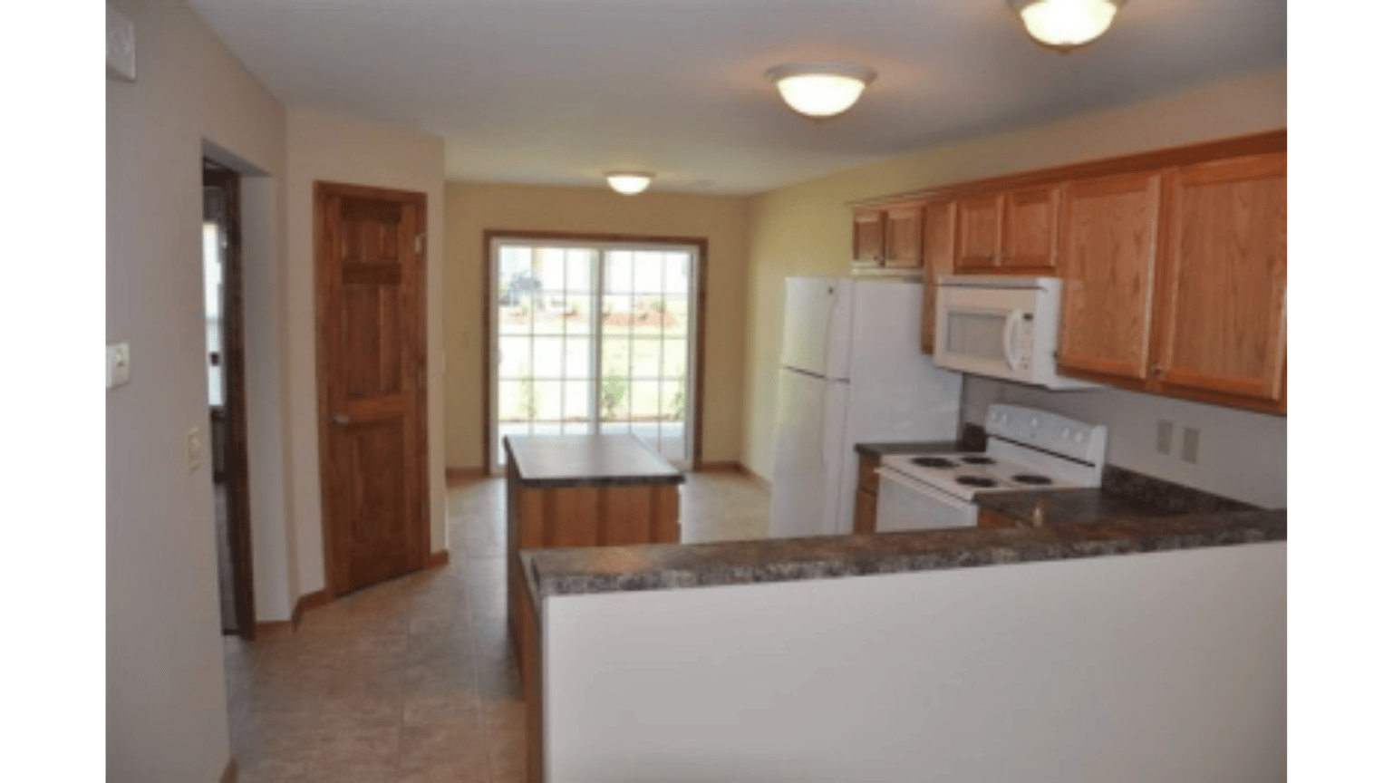 An empty kitchen with wooden cabinets and a white refrigerator