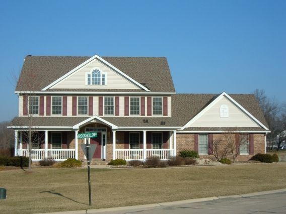 A large house with a large porch and a green street sign in front of it