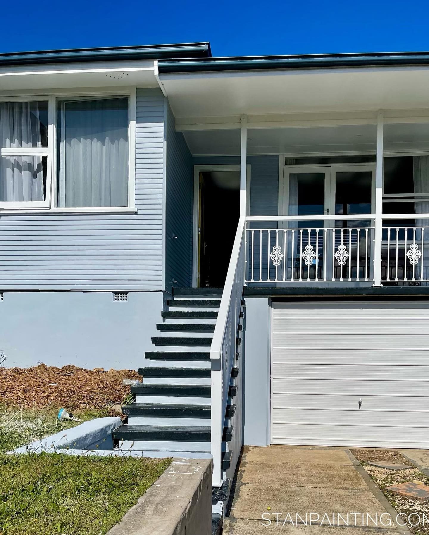 Blue House with White Trim, Porch, and Garage Door Under a Blue Sky — Stan Painting Services In Thornton, NSW