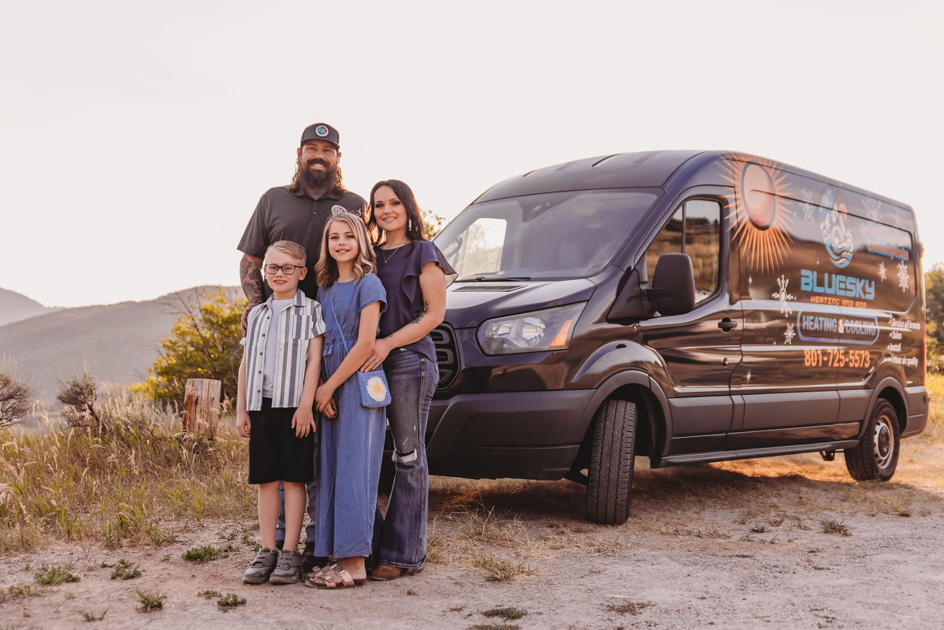 Family standing beside a black van in a desert landscape at sunset