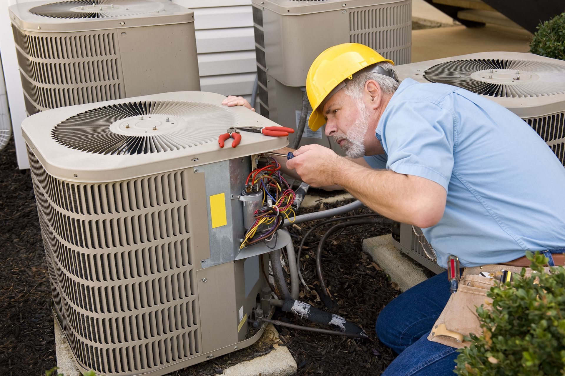 Technician in hard hat repairs outdoor HVAC units beside several rooftop condensers.