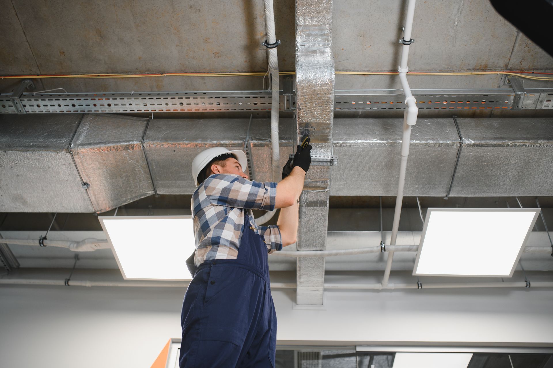 Worker in blue overalls inspecting a metal beam on an industrial ceiling.