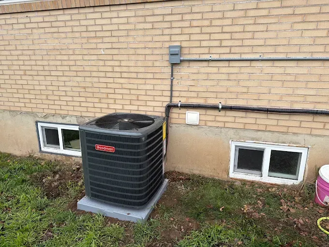 Outdoor air conditioning unit beside a brick house with utility lines and basement windows
