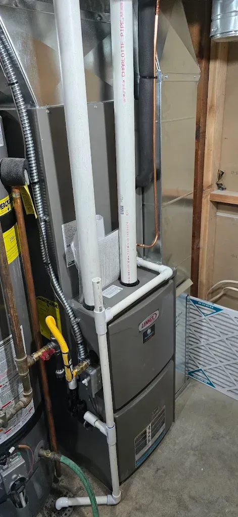 Basement utility area with furnace, white pipes, and a yellow-and-black hand truck beside a concrete wall.