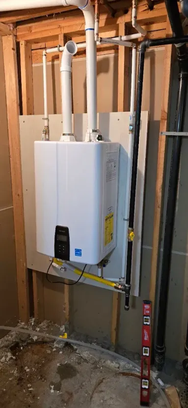 White wall-mounted water heater in an unfinished basement with exposed pipes and framing.