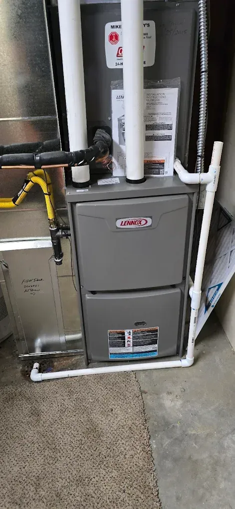 Residential furnace and water heater in a utility closet with exposed pipes and concrete floor.