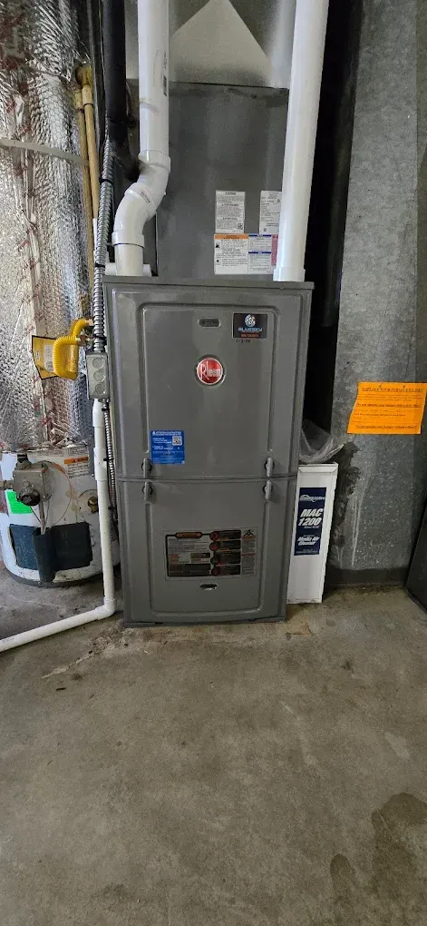 Gray HVAC furnace in a basement, with exposed ductwork and a concrete floor.