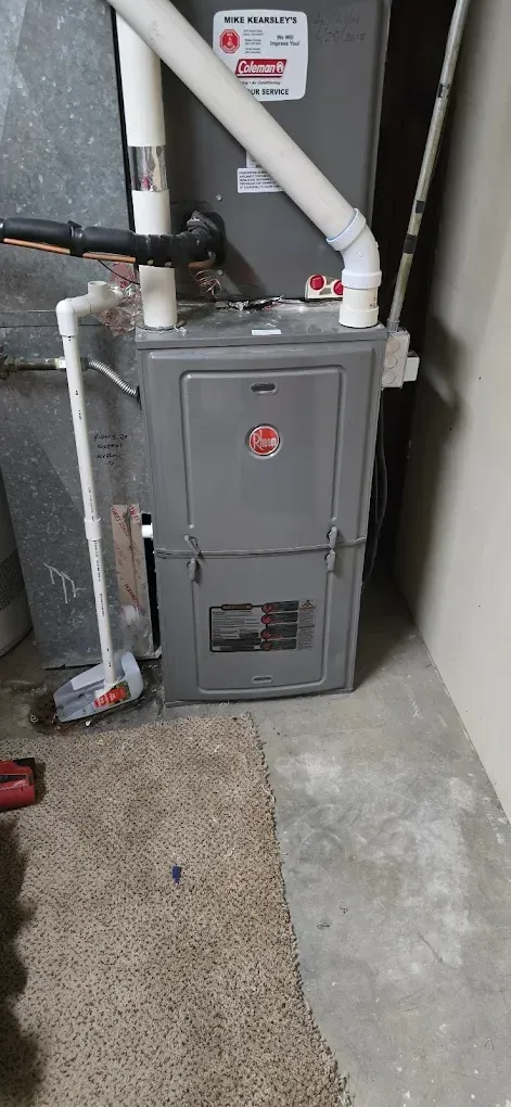 Gray furnace with white PVC vent pipes in a basement utility area next to a rug and concrete floor