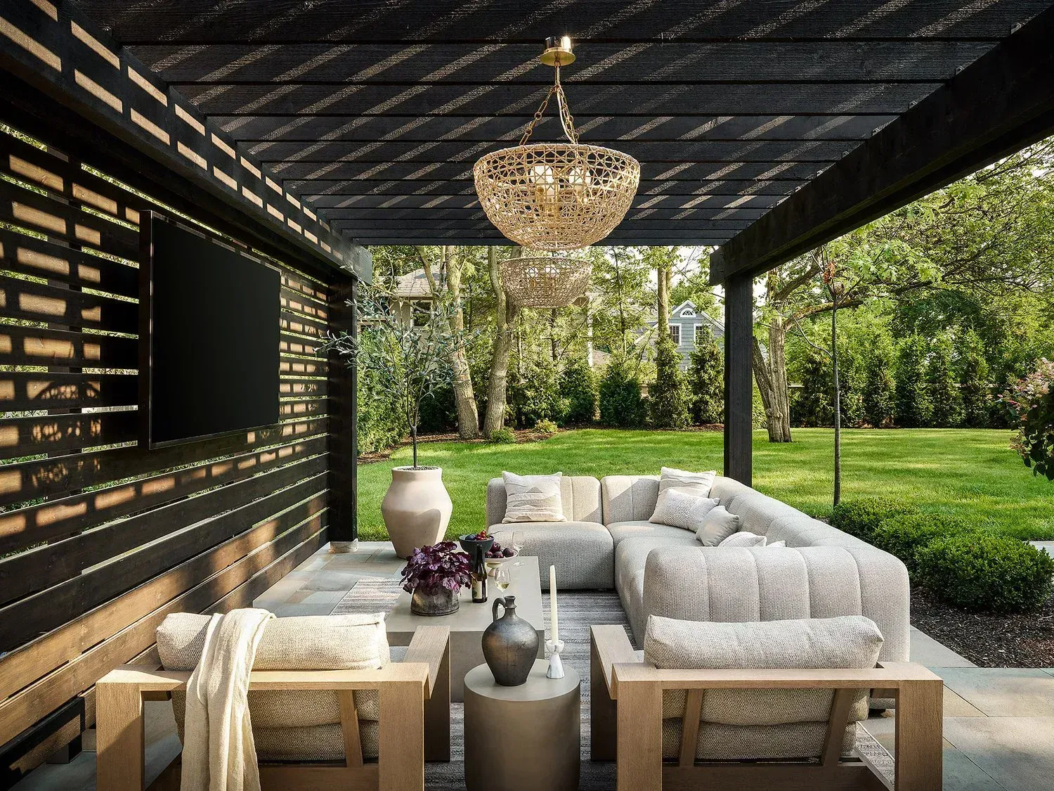 Best Landscaper in Colts Neck NJ. Modern outdoor patio lounge with gray sofas, chandelier, and garden view under a covered pergola