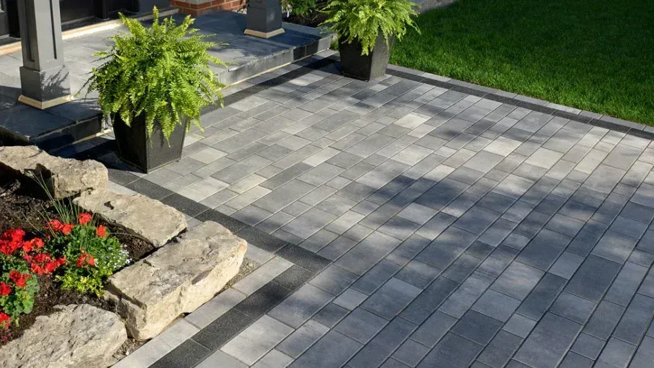 paver patio in Rumson NJ. Gray stone patio with potted fern, flower bed, and green lawn beside steps and columns.