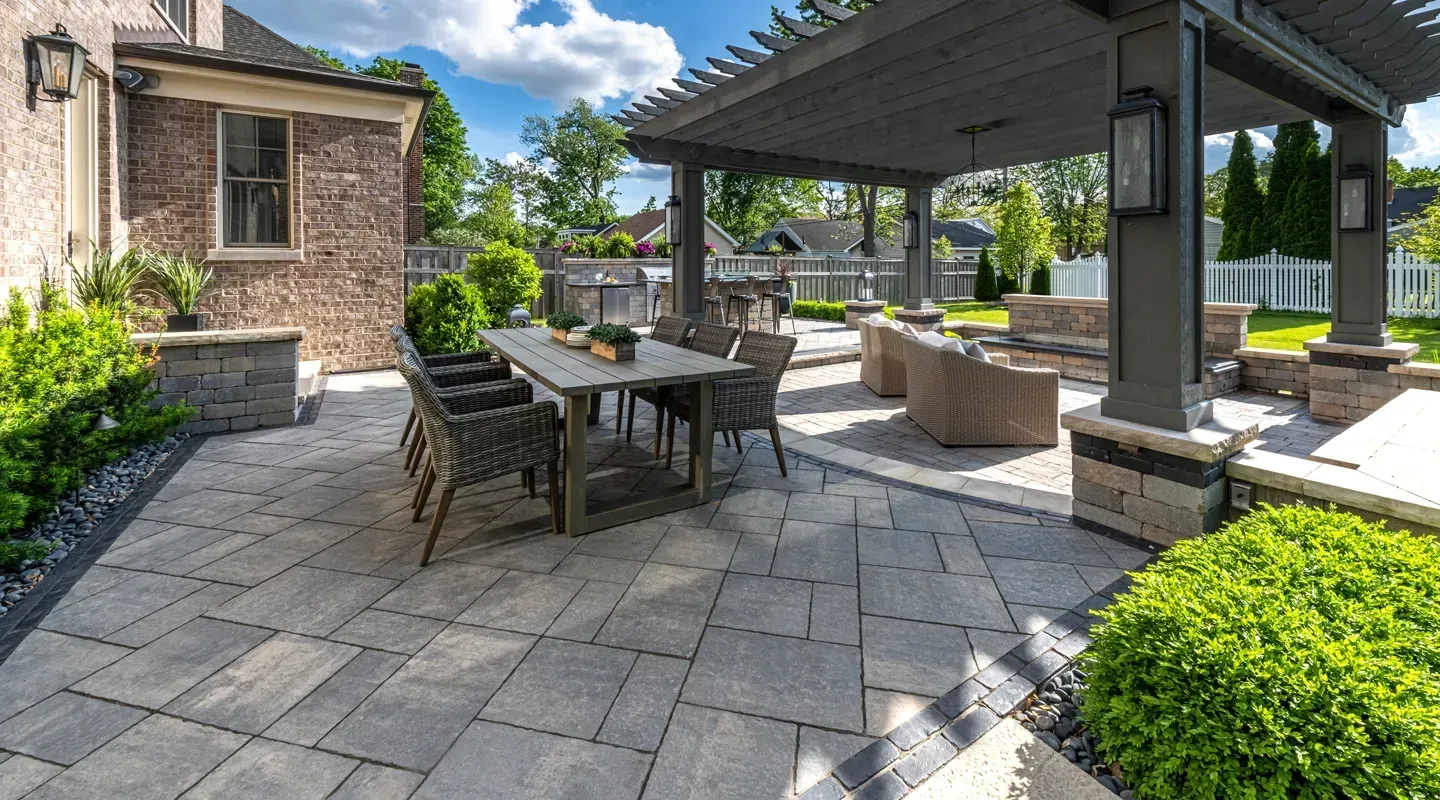 Patio with stone paver in Holmdel is, outdoor dining table, covered seating area, and manicured shrubs beside a brick building
