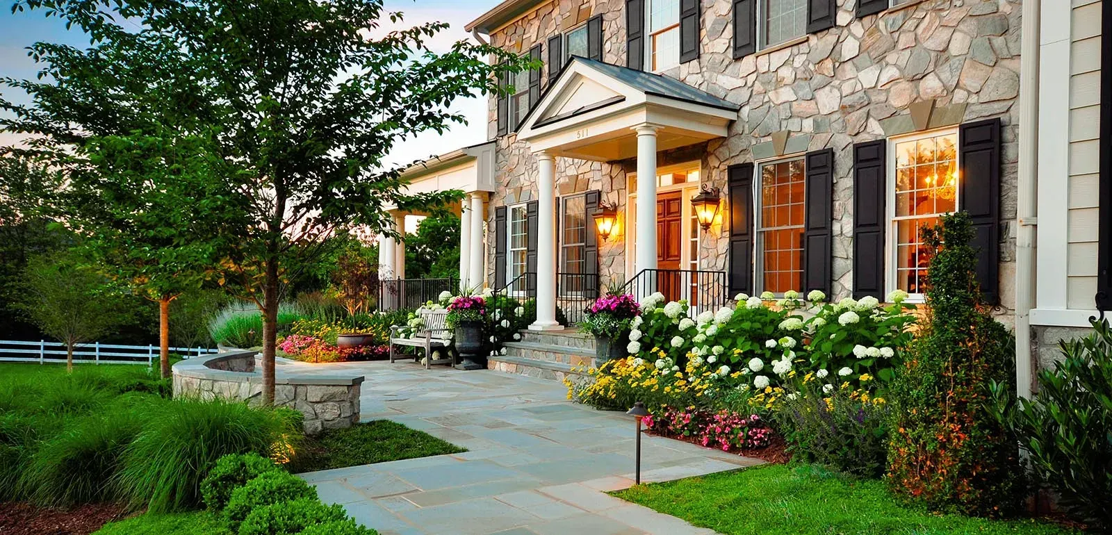 Landscape in Fair Haven NJ.Stone house entrance with lit porch, flower beds, and a curving garden walkway