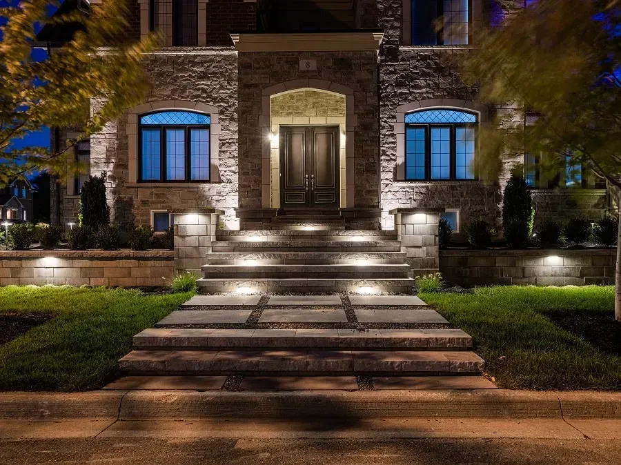 local landscape lighting in Monmouth County NJ. Lit stone house entrance at night with illuminated steps, blue windows, and landscaped front yard