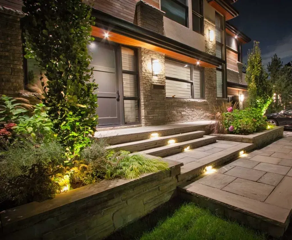 Landscape Lighting company in Manalapan NJ. Modern house entrance at night with lit steps, landscaped garden, and stone walkway