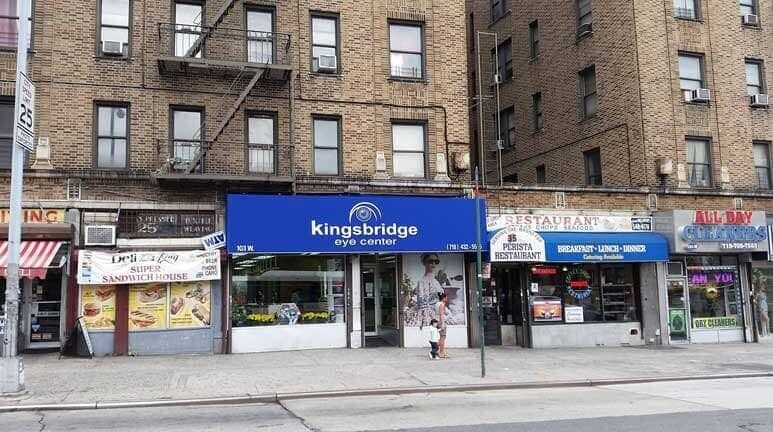 Street-level view of storefronts, including a blue Kingsbridge deli sign on a brick apartment building.