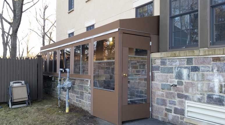 Covered building entrance with brown metal awning and glass doors beside a stone wall
