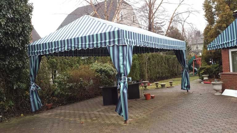 Blue-and-white striped canopy tent in a paved courtyard with potted plants and a house entrance